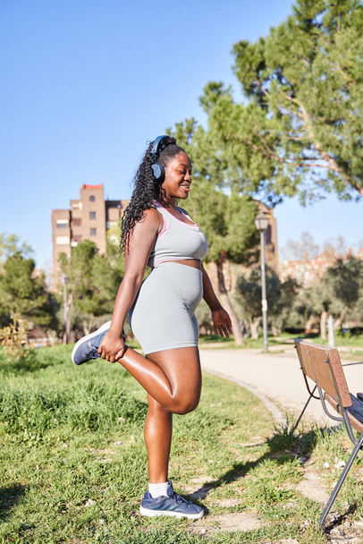 Junge Frau streckt sein Bein beim Aufwärmen vor dem Outdoor-Lauftraining. Die Frau in Sportbekleidung trainiert morgens draußen für Gesundheit und Wohlbefinden. - Foto, Bild