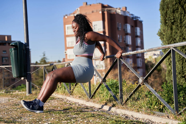 Treino matinal. afro-americana mulher formação tríceps encostado em um corrimão. - Foto, Imagem