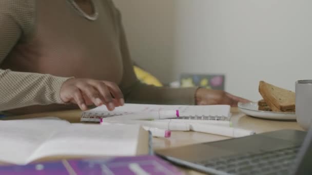 Cintura hacia arriba de la joven mujer afroamericana sentada en la mesa con materiales de estudio, libros de texto y computadora portátil en ella para hacer la asignación del hogar para la universidad, viviendo en el apartamento con la compañera de cuarto blanca - Metraje, vídeo