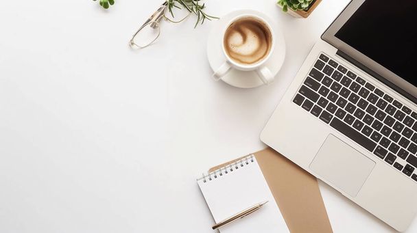 Moderner Arbeitsplatz mit Laptop, Kaffeetasse, Notizbuch, Stift und Brille auf weißem Schreibtisch. - Foto, Bild