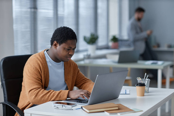 Młody poważny Afroamerykanin męski przedsiębiorca wpisując na klawiaturze laptopa podczas pracy nad nowym projektem lub organizacji pracy - Zdjęcie, obraz
