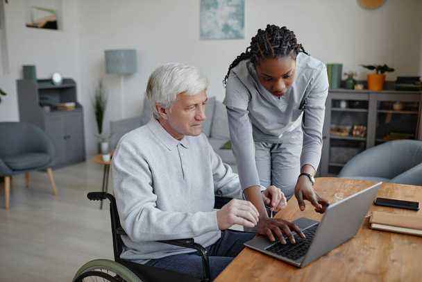 A fogyatékossággal élő idős ember portréja, aki a gondozását segítő nővérrel vagy gondozóval tanul számítógépet használni - Fotó, kép