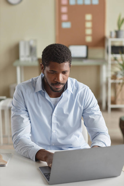 Vertical portrait of handsome black man as businessman using computer at desk in office - Photo, Image