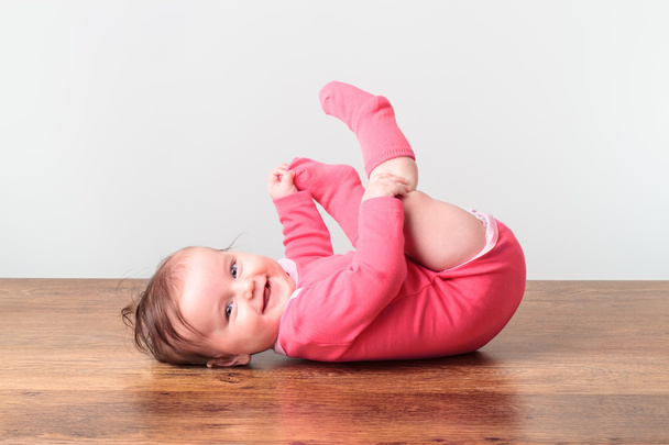 Smiling little baby girl playing with her feet - Foto, Imagem
