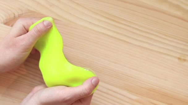 Girl kneads yellow slime against the background of a table. Woman's hands stretch bright yellow slime close-up. An anti-stress toy for relaxation, a way to escape. A fun sensory activity - Footage, Video