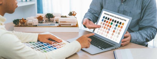 Επαγγελματίας αρχιτέκτονας παρουσιάζει επιλογή χρωμάτων με τη χρήση laptop εμφανίζεται το χρώμα, ενώ η γυναίκα σχεδιαστής εσωτερικών χώρων επιλέγει το υλικό κουρτίνας. Δημιουργική εργασία και ομαδική εργασία. Ποικιλία. - Φωτογραφία, εικόνα