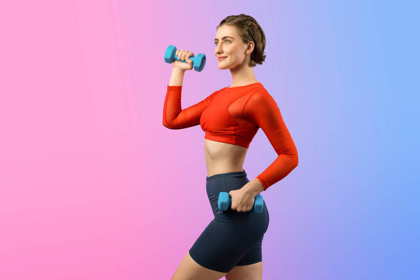Full body length gaiety shot athletic and sporty woman with dumbbell for weight lifting as bodybuilding exercise in standing posture on isolated background. Healthy active and body care lifestyle - Photo, Image