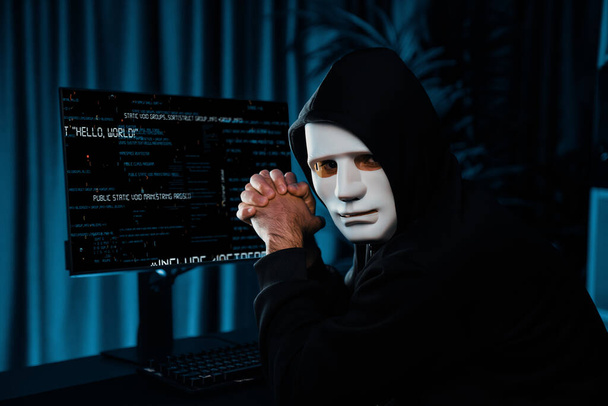 ホワイト犯罪者の匿名マスクは,コンピュータのランサムウェア上のメインデータベースサーバードライブを介してハッキングプログラミングによるコディングウイルスのインストール画面でカメラを見ているデスク上の喜びの手をマスクします. サーモス. - 写真・画像