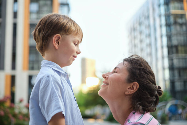 Adorable mother and son smiling happy having fun at city background. Motherhood concept, hugging. Boy 8 years old with mother in bright clothes enjoying summer day. High quality photo - Photo, Image