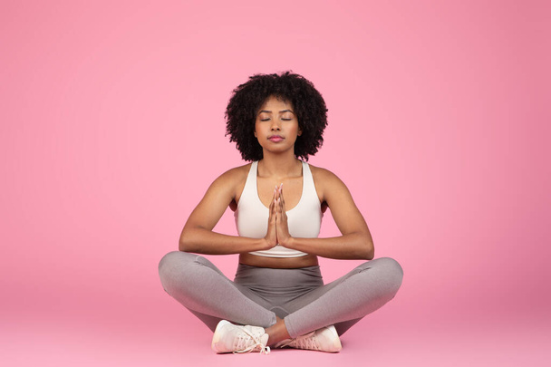 Spokojna Afroamerykanka siedząca w pozycji do medytacji, promująca spokój i spokój ducha, odizolowana na różowo - Zdjęcie, obraz