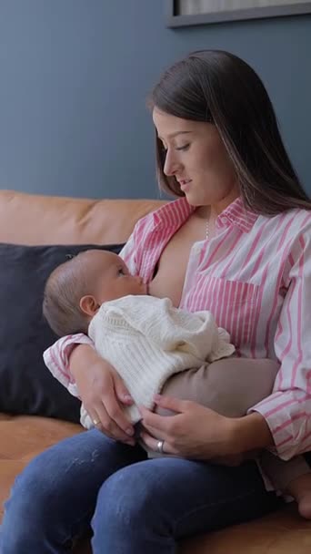 Giovane madre che parla con sua figlia durante l'allattamento, seduta nel soggiorno della sua casa - Filmati, video