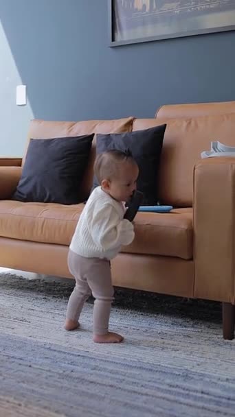 Το μωρό κάνει τα πρώτα του βήματα ενώ στέκεται στον καναπέ στο σπίτι - Πλάνα, βίντεο