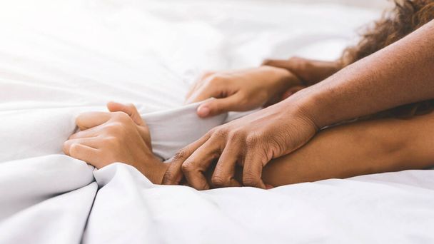 ベッドの情熱。エクスタシー、クローズ アップで白いシーツを引っ張ってアフリカ系アメリカ人のカップルの手 - 写真・画像