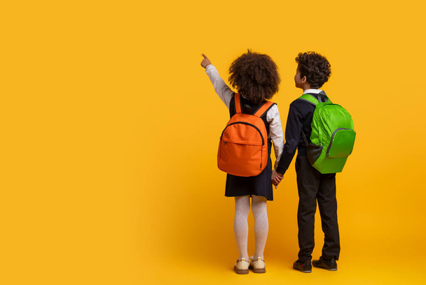 Los hermanos afroamericanos con trajes escolares tomados de la mano sobre un fondo amarillo representan la infancia y el vínculo entre los negros. espacio de copia, vista trasera - Foto, Imagen