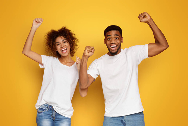 Éxito alegre pareja afroamericana levantando las manos en feliz asombro, fondo naranja
 - Foto, Imagen