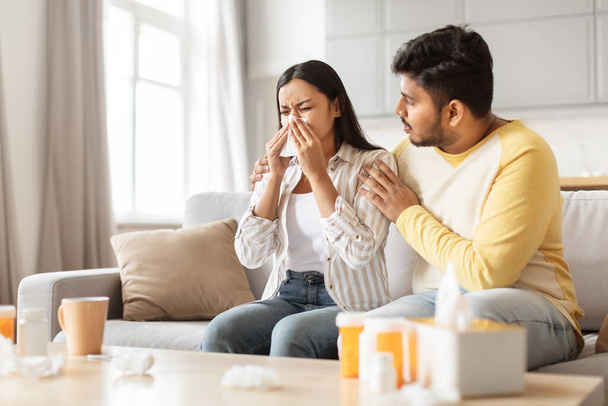 An Indian couple at home, the man comforting his sneezing spouse, depicting millennials managing health together - Photo, Image