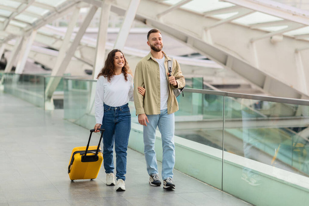 Ένας χαρούμενος άντρας και μια γυναίκα περπατούν σε ένα αεροδρόμιο, ο άντρας που έχει διαβατήρια και κάρτες επιβίβασης, ζευγάρι που απολαμβάνει να ταξιδεύει μαζί. - Φωτογραφία, εικόνα