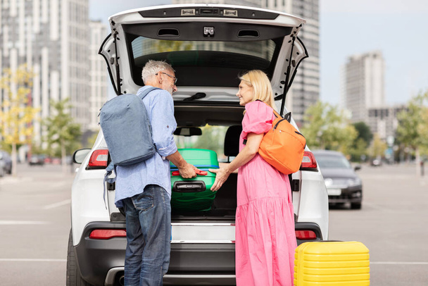 Um casal aposentado coloca sua bagagem no porta-malas de seu carro, simbolizando a liberdade e a atividade da vida sênior. - Foto, Imagem