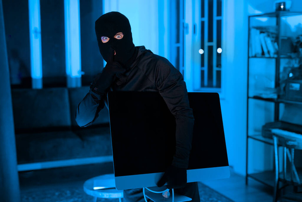 Eine nächtliche Wohnzimmerszene, in der ein Einbrecher beim Diebstahl eines großen Fernsehers erwischt wird, unterstreicht das Thema Wohnungsdiebstahl - Foto, Bild
