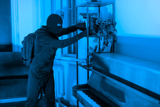 In einer schwach beleuchteten Wohnung wird ein Dieb beim Diebstahl von Wertgegenständen aus einem Schrank ertappt, was einen stillen Einbruch in der Nacht illustriert - Foto, Bild