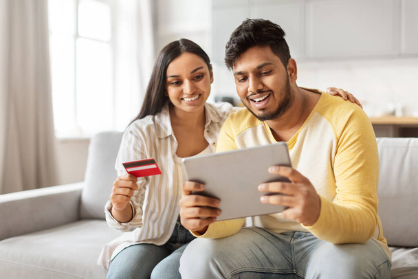 Egy indiai házaspár kényelmesen ül otthon, a férj hitelkártyát tart, a feleség pedig táblát tart a kezében, példázva a modern Y-generációs keleti vásárlási szokásokat. - Fotó, kép