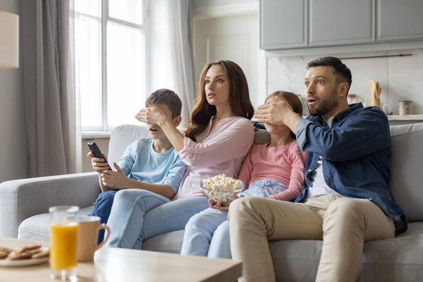 Evropská rodina vykazuje různé reakce šoku, zvědavosti a zábavy na scénu na obrazovce, ztělesňující lásku a blízké vztahy v domácím prostředí - Fotografie, Obrázek