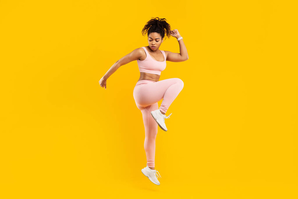 Vilkas kuva afrikkalainen amerikkalainen nainen ilmassa fitness rutiini, jossa energiaa ja eloisuutta, eristetty keltaista taustaa vasten - Valokuva, kuva