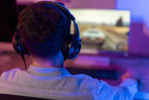 De man gamer is diep geabsorbeerd in zijn spel, achtergrondverlichting zijn figuur te midden van de donkere kamers sfeer - Foto, afbeelding