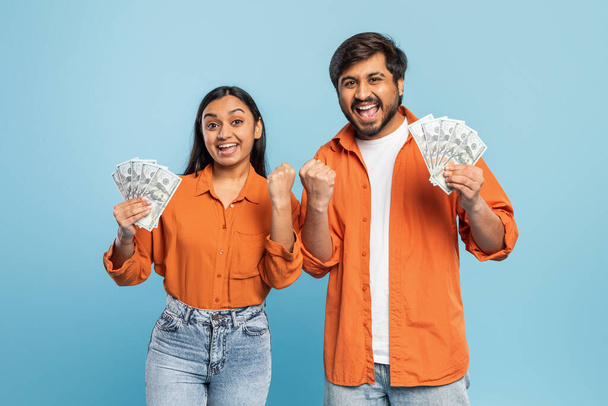 Індійський чоловік і жінка захоплено тримають і показують готівку, символізуючи фінансовий успіх або перемагають на синьому - Фото, зображення