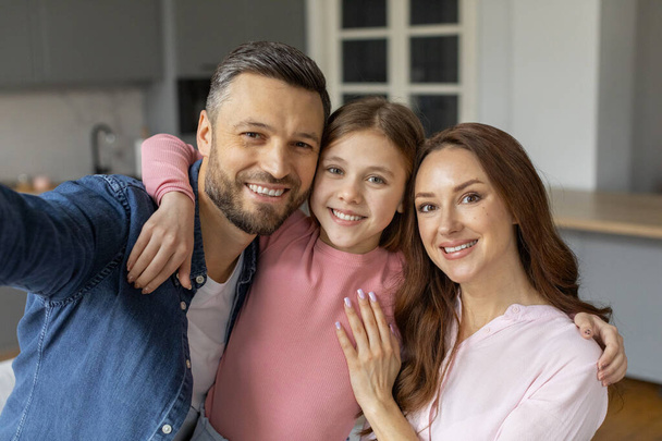 Egy közeli kép egy mosolygó családról, ami egy férfiból, egy fiatal lányból és egy nőből áll, valószínűleg a konyhájukban. - Fotó, kép