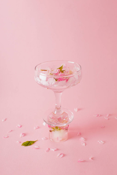 ピンクの背景の花と氷のキューブに立っているバラの花が付いたカクテルグラス. - 写真・画像