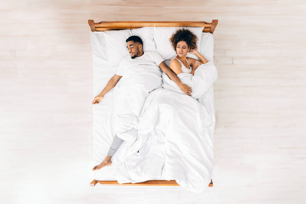 Άβολο όνειρο. Αναστατωμένη μαύρη γυναίκα που υποφέρει από τον απλωμένο άντρα της στο κρεβάτι, πάνω όψη με κενό χώρο - Φωτογραφία, εικόνα