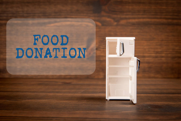 Lebensmittelspenden. Miniatur-Kühlschrank auf einem hölzernen Texturhintergrund. - Foto, Bild