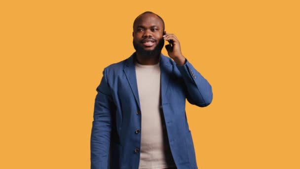 Joyous man with positive emotion, enjoying talking with friends phone call using smartphone, studio background. Happy african american person with smile on face during telephone call, camera B - Footage, Video