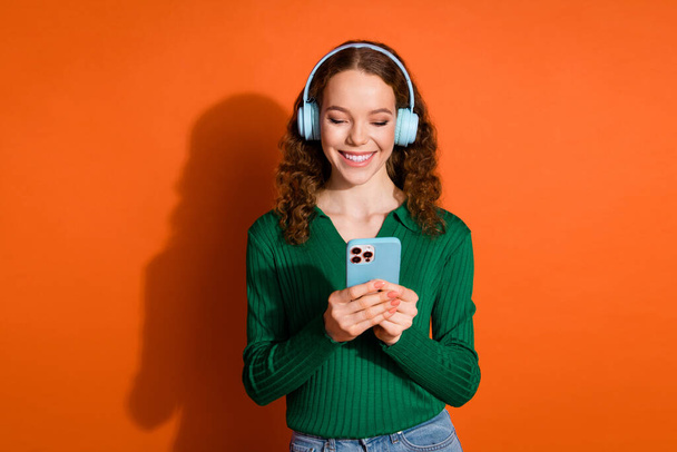 Photo of excited cheerful lady dressed green shirt headphones listening music modern device isolated orange color background. - 写真・画像