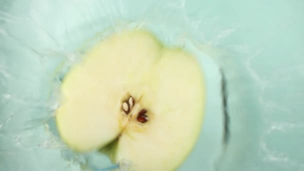 Μήλο μισό πέφτει στο νερό από πάνω, δημιουργώντας μια βουτιά. Καθώς το μήλο βυθίζεται, οι κυματισμοί απλώνονται όμορφα. Μήλα εισόδου στο νερό συλλαμβάνεται με εκπληκτική λεπτομέρεια συλλαμβάνονται με μεγάλη λεπτομέρεια - Πλάνα, βίντεο