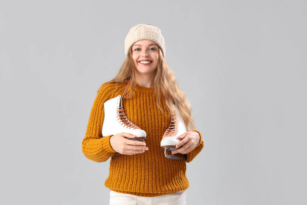 Joyeux beau jeune femme en pull chaud avec patins à glace sur fond gris - Photo, image