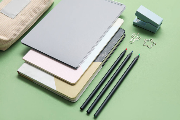 Caso lápis bege com diferentes artigos de papelaria escolar e cadernos em fundo verde - Foto, Imagem
