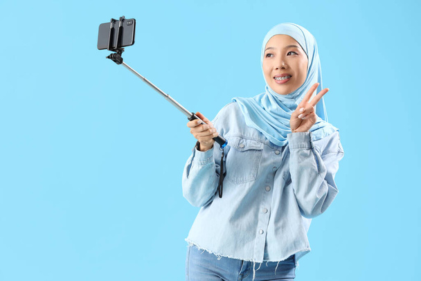 Hermosa joven asiática en hijab tomando selfie sobre fondo azul - Foto, imagen