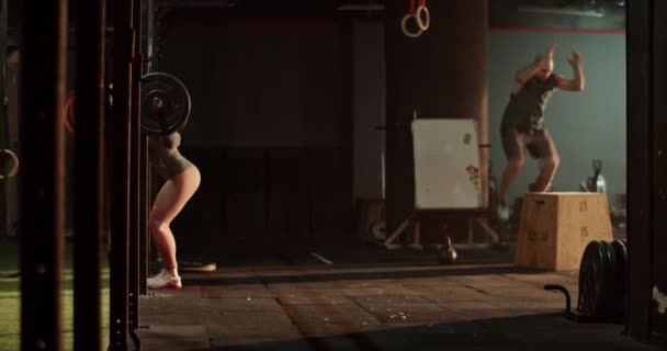 V reálném čase boční pohled sportovkyně dívá pryč při cvičení s těžkým činka a trénink s mužem skákání na blokovat ze země v zadní s jasným slunečním světlem - Záběry, video