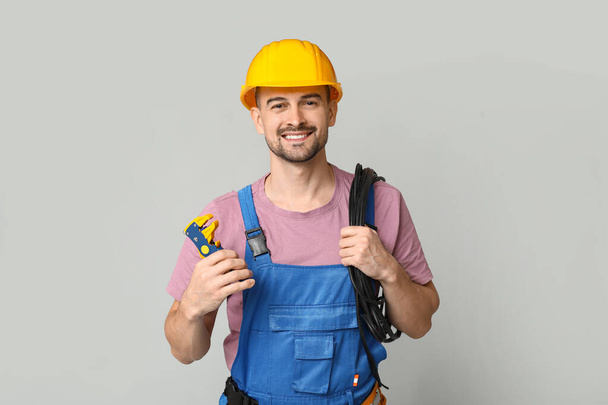 Portrait of male electrician with crimper and wires on grey background - Photo, Image