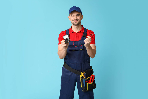 Retrato de electricista masculino con multímetro sobre fondo azul - Foto, Imagen