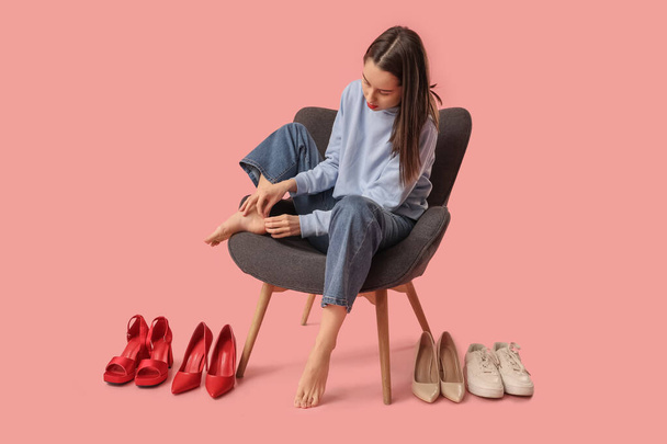 Fiatal nő, különböző cipők alkalmazása kötés a lábát, miközben ül a karosszéken szemben rózsaszín háttér, közelkép. Kényelmetlen cipő koncepció - Fotó, kép