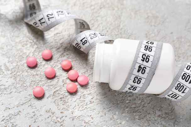 Пляшка з таблетками для схуднення та вимірювальною стрічкою на сірому гранжевому фоні - Фото, зображення