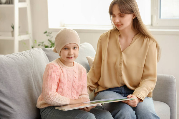 Κοριτσάκι μετά τη χημειοθεραπεία με τη μητέρα της να διαβάζει βιβλία στο σπίτι. Διεθνής Ημέρα κατά του καρκίνου της παιδικής ηλικίας - Φωτογραφία, εικόνα