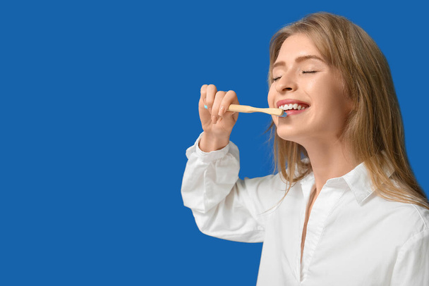 Νεαρή γυναίκα βουρτσίζει τα δόντια της σε μπλε φόντο - Φωτογραφία, εικόνα