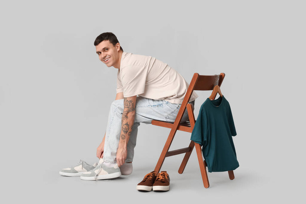 Handsome young man and chair with clothes on grey background - Фото, изображение