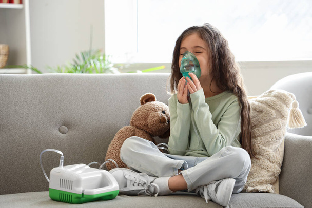 Bambina che usa il nebulizzatore sul divano di casa - Foto, immagini