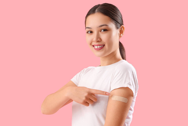 Schöne junge Frau zeigt auf ein medizinisches Pflaster auf ihrem Arm vor rosa Hintergrund - Foto, Bild