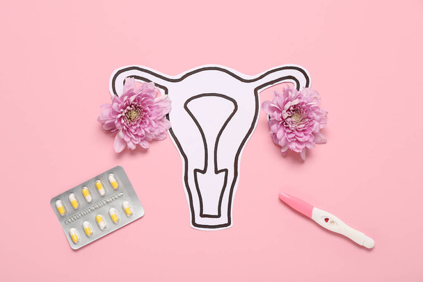Papier-Uterus mit Chrysanthemenblüten, Schwangerschaftstest und Pillen auf rosa Hintergrund - Foto, Bild